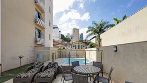 A rooftop patio with a pool, lounge chairs, and a dining table. - BH Jaraguá Hotel (Belo Horizonte)