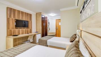 A hotel room with two beds, a desk with a flat-screen TV, a small refrigerator, and a wooden headboard.