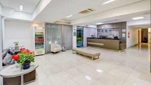 A modern hotel lobby with a reception desk, seating area, and a refrigerator stocked with beverages. - BH Jaraguá Hotel (Belo Horizonte)
