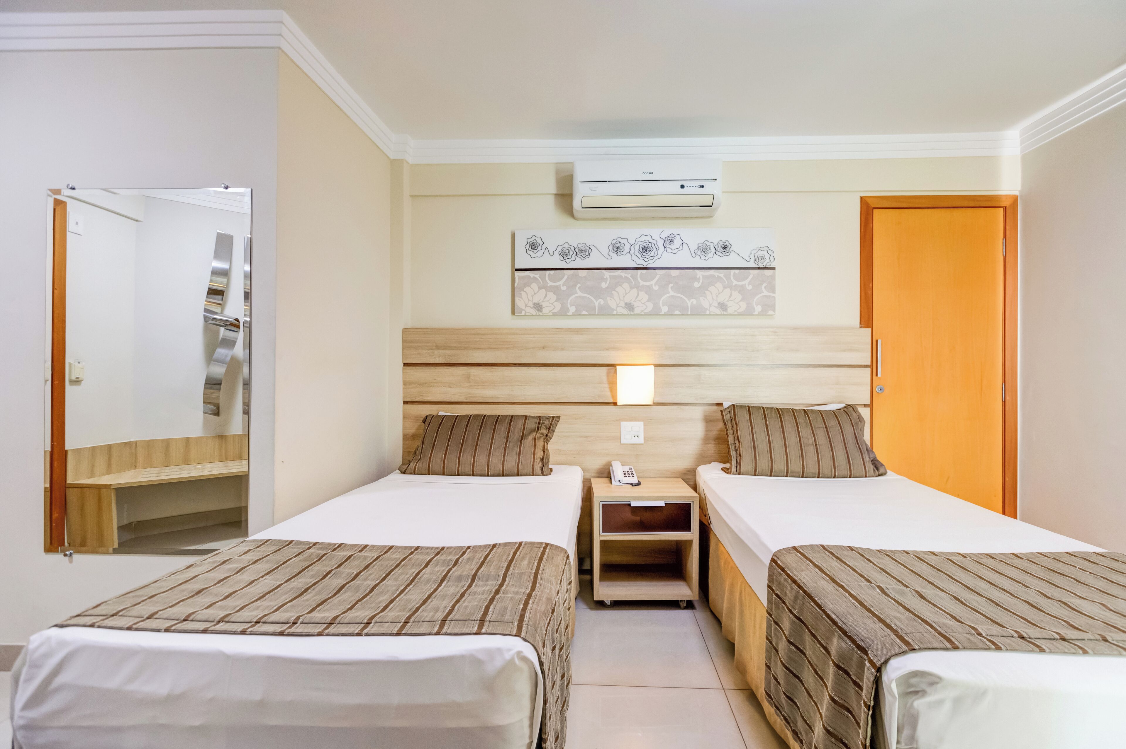 A hotel room with two beds, a bedside table with a phone, an air conditioning unit, and a mirror.
