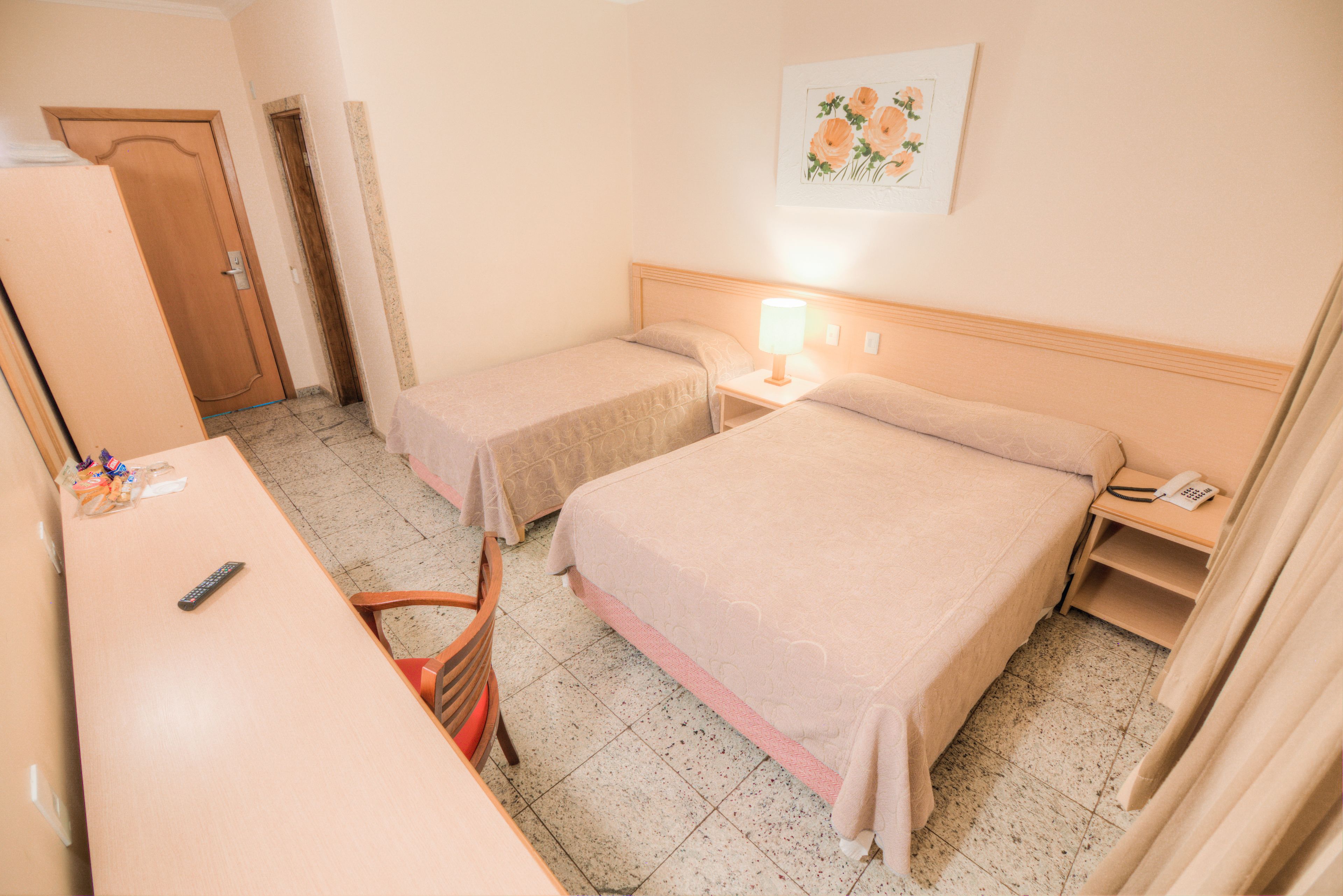 A hotel room with two beds, a desk, a chair, a telephone, and a painting on the wall.