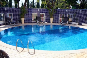 Una piscina al aire libre, sombrillas, sillones reclinables de piscina