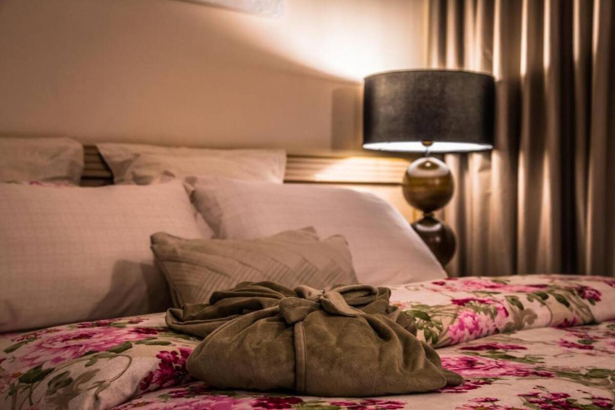 Una cama bien hecha con una colcha estampada con motivos florales, una lámpara y un bolso sobre la cama.