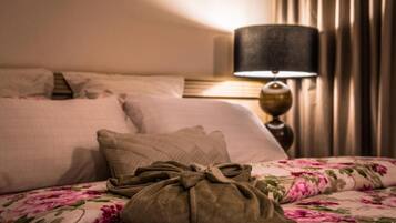 Una cama bien hecha con una colcha estampada con motivos florales, una lámpara y un bolso sobre la cama.