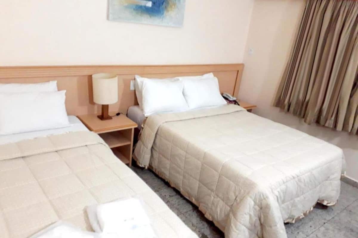 Una habitación de hotel con dos camas, una mesita de noche, una lámpara y un cuadro en la pared.