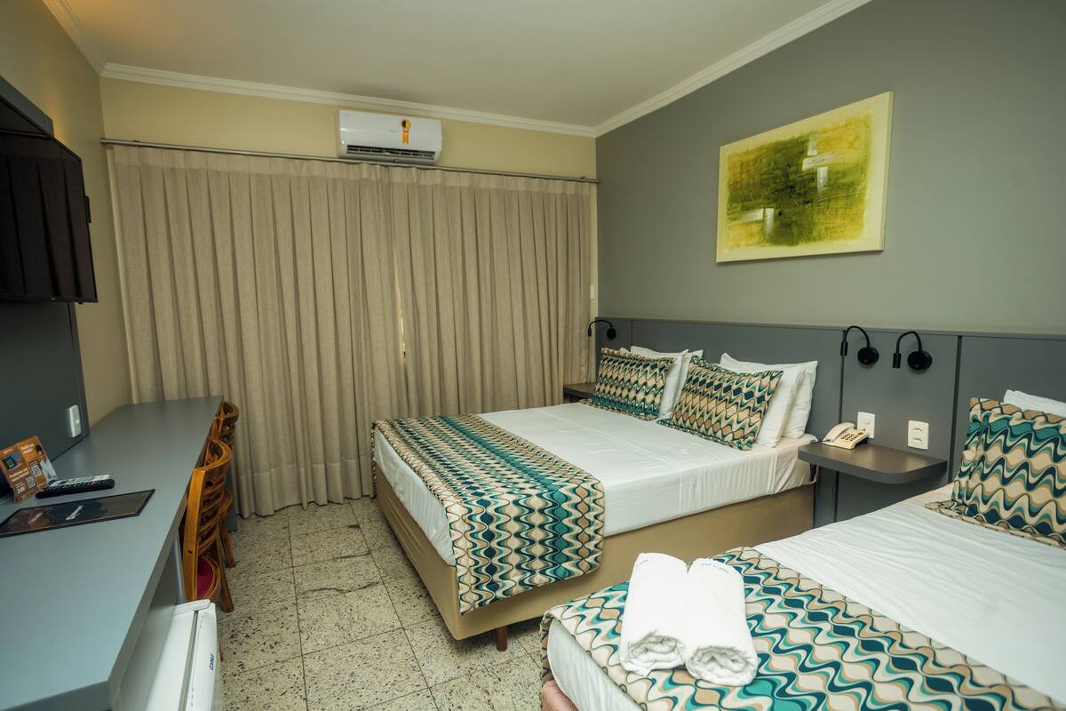 Habitación de hotel con dos camas, un escritorio, una silla, aire acondicionado, un cuadro en la pared y un teléfono en la mesita de noche.
