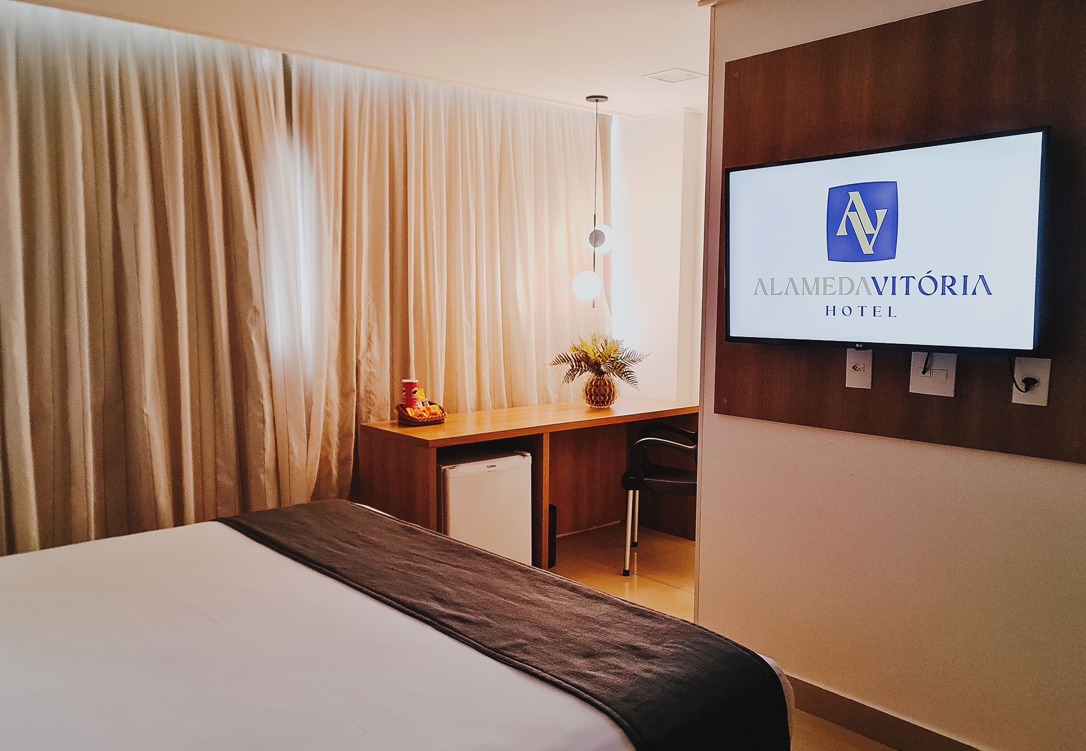 Une chambre d’hôtel avec un lit, un bureau, une chaise, une télévision et un rideau.