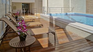A poolside area with wooden flooring, lounge chairs, and a small table with a potted orchid. - Alameda Vitória Hotel (Vitoria)