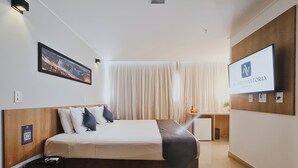 A hotel room with a bed, a desk, a TV, and a window with curtains. - Alameda Vitória Hotel (Vitoria)