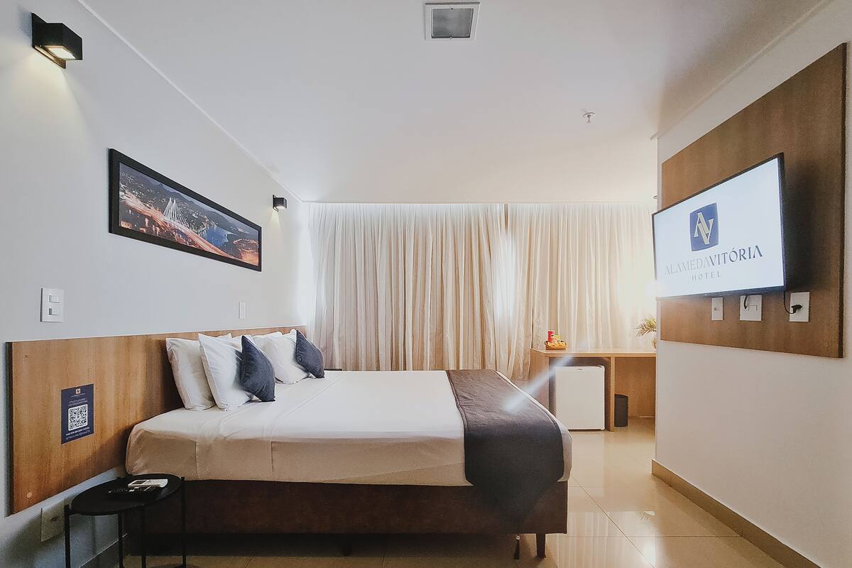 A hotel room with a bed, a desk, a TV, and a window with curtains.