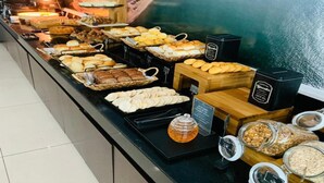 A buffet with various food items and a view of a coastal cityscape. - Alameda Vitória Hotel (Vitoria)