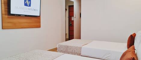 A hotel room with two beds, a TV mounted on the wall, and an air conditioning unit.