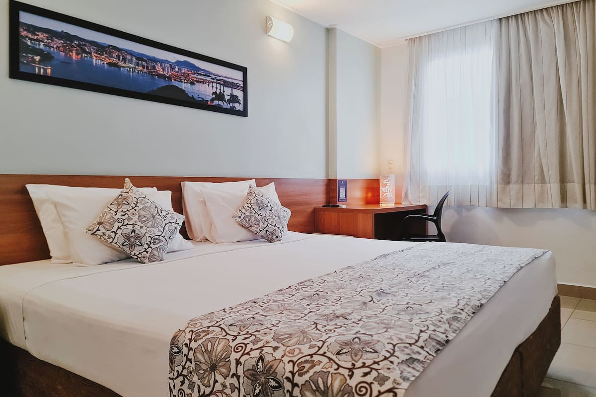 A hotel room with a large bed, two pillows, a nightstand, a desk, and a chair.
