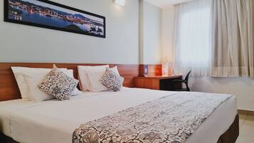 A hotel room with a large bed, two pillows, a nightstand, a desk, and a chair.
