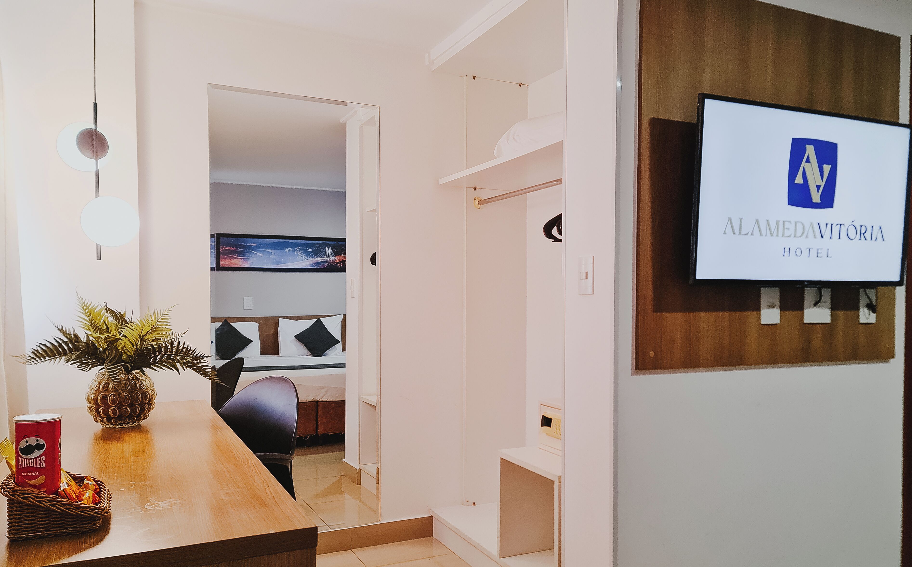 Zona de recepción de hotel con diseño moderno, un mostrador de recepción, un televisor mostrando el nombre del hotel y una vista de la distribución de las habitaciones al fondo.