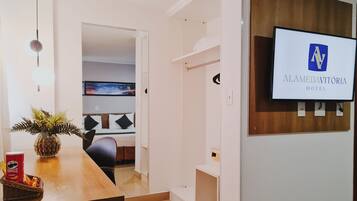 Zona de recepción de hotel con diseño moderno, un mostrador de recepción, un televisor mostrando el nombre del hotel y una vista de la distribución de las habitaciones al fondo.