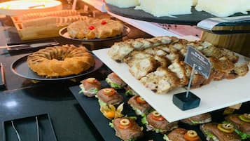 Un bufé con diversos alimentos, incluyendo un pastel Bundt, pan en rebanadas y sándwiches.