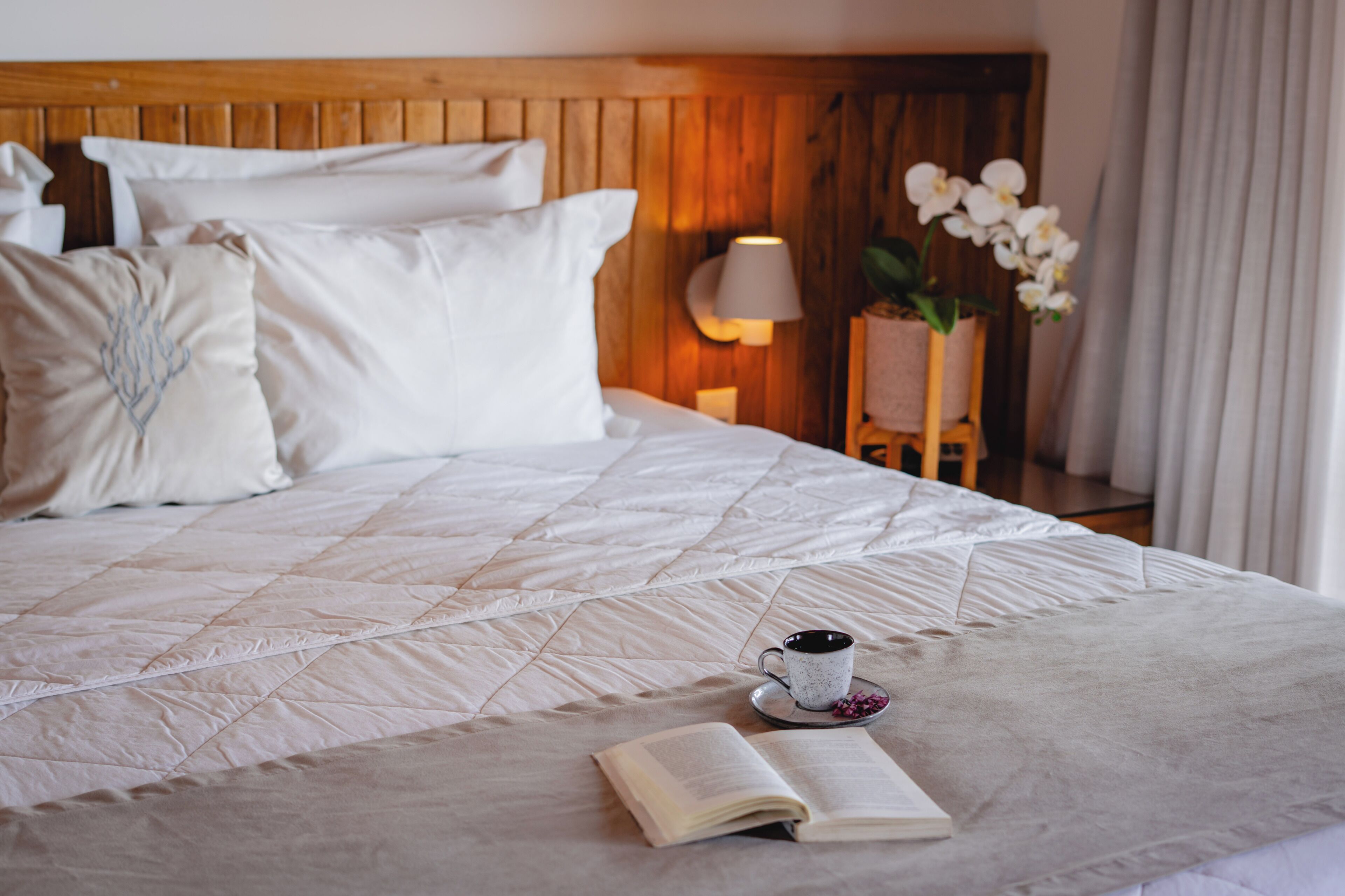 A neatly made bed with a quilted cover, a cup of coffee, and an open book on the bed.