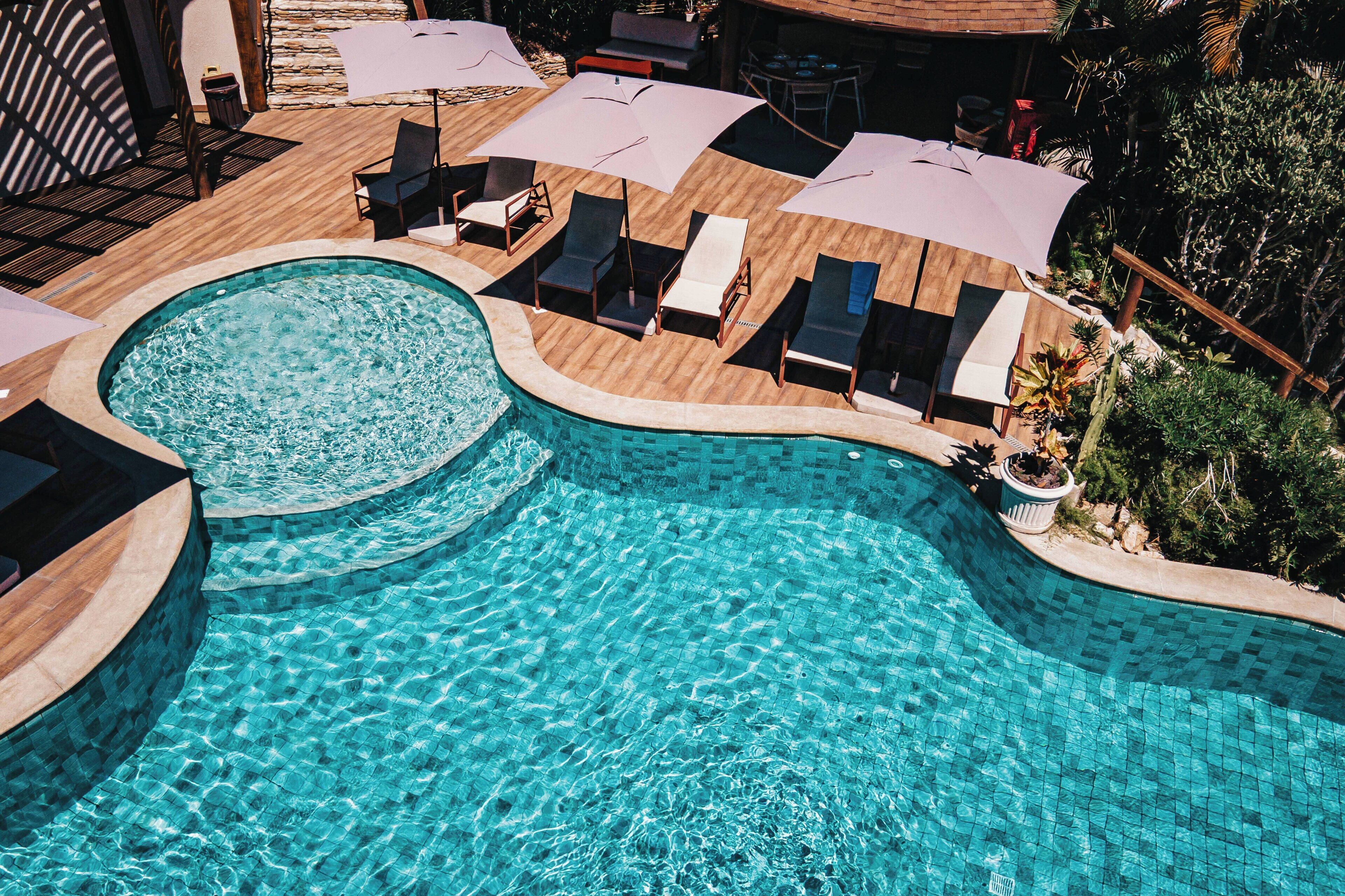 A swimming pool with lounge chairs and umbrellas, surrounded by wooden decking and greenery.
