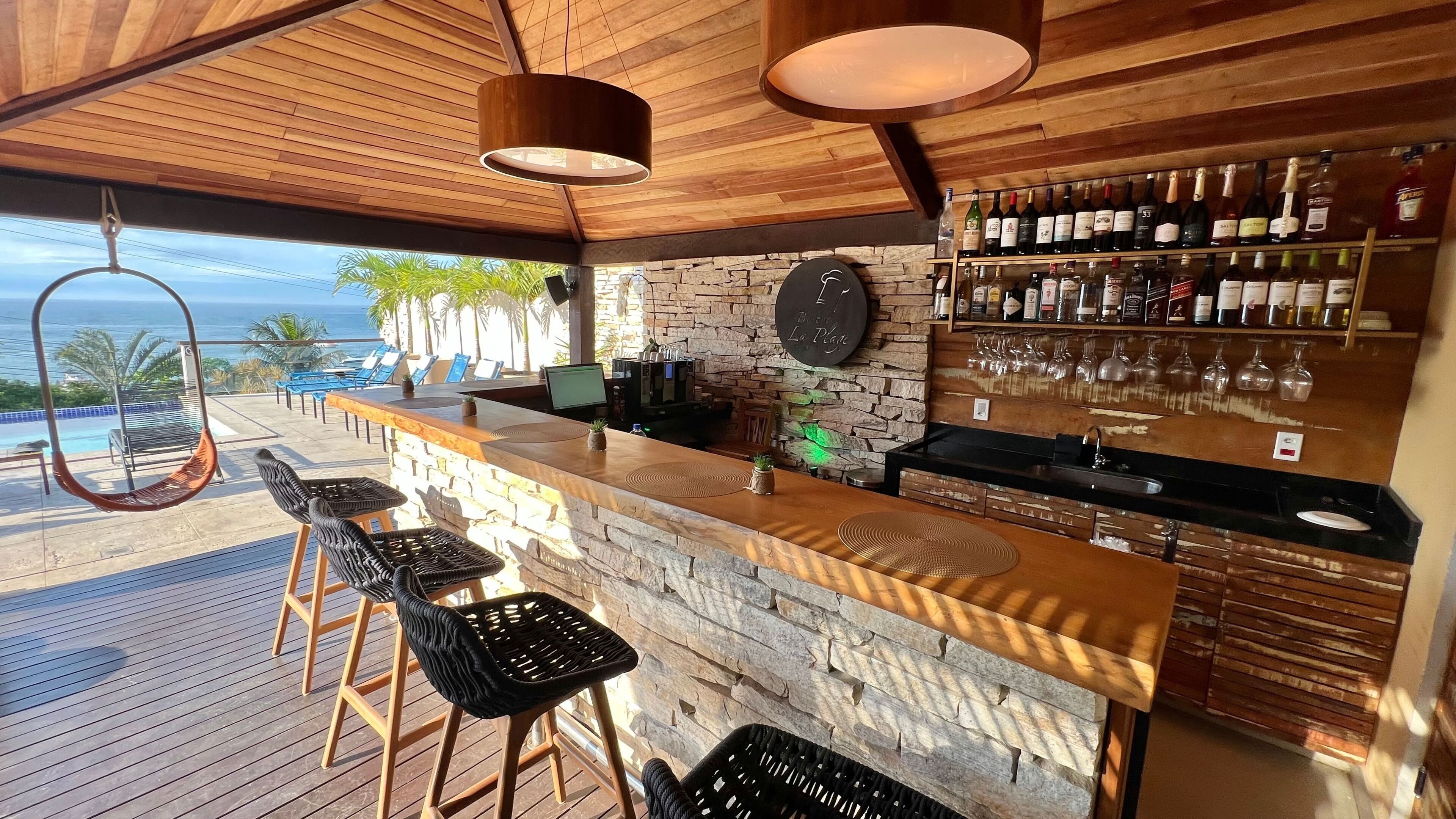 A bar area with a stone wall, wooden ceiling, and a view of the ocean.