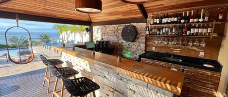 A bar area with a stone wall, wooden ceiling, and a view of the ocean.