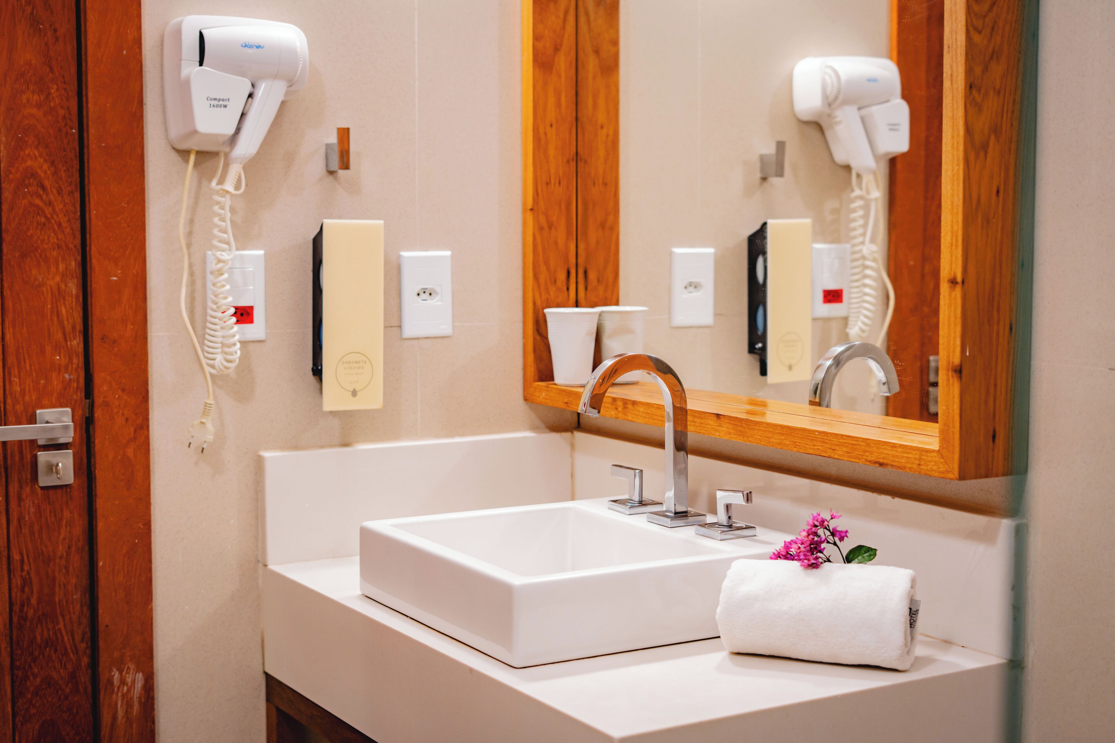 A bathroom with a white sink, a wooden vanity, a mirror with a wooden frame, and two hair dryers mounted on the wall.