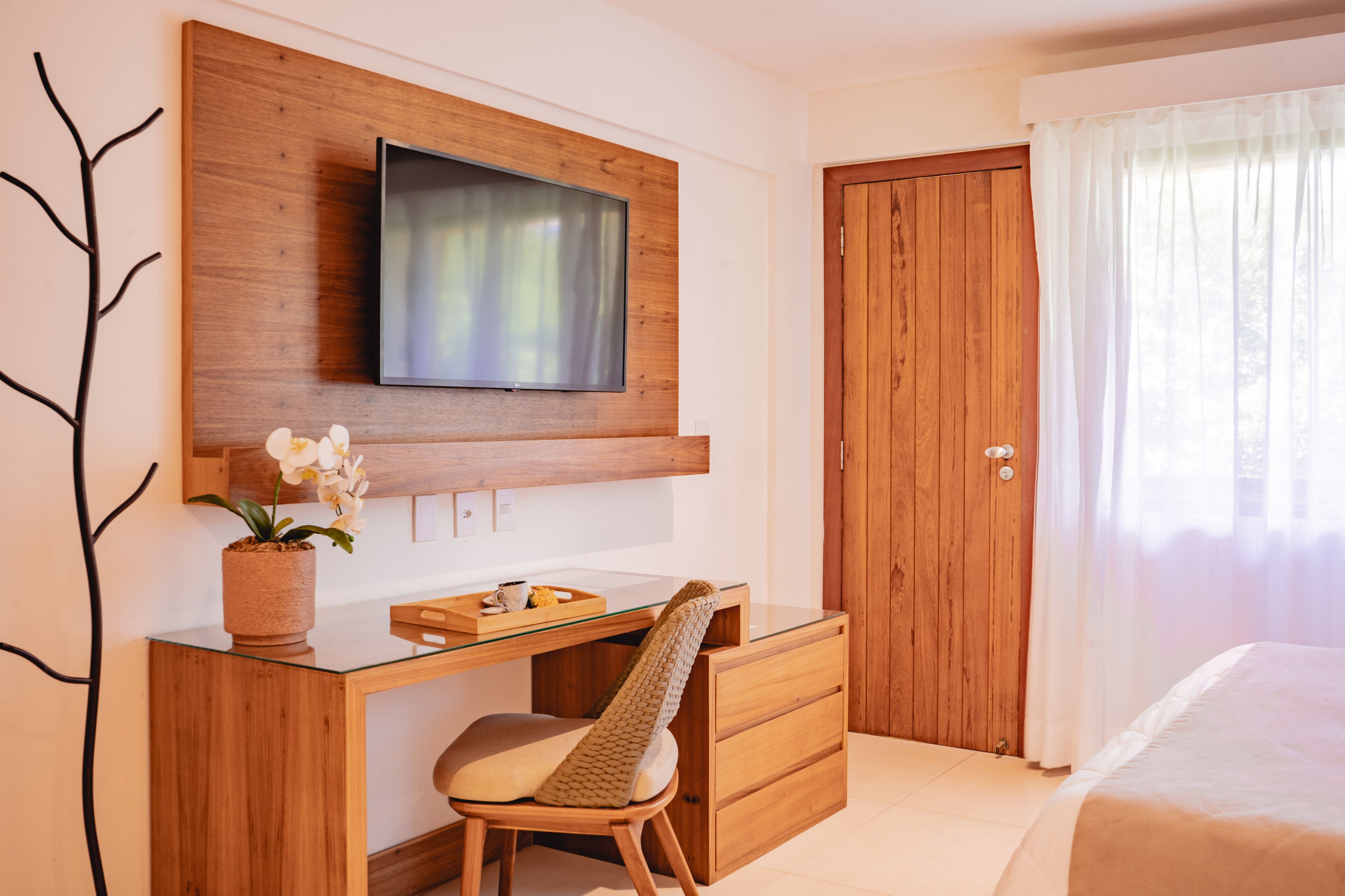 Quarto com escrivaninha de madeira, cadeira, televisão e cama.