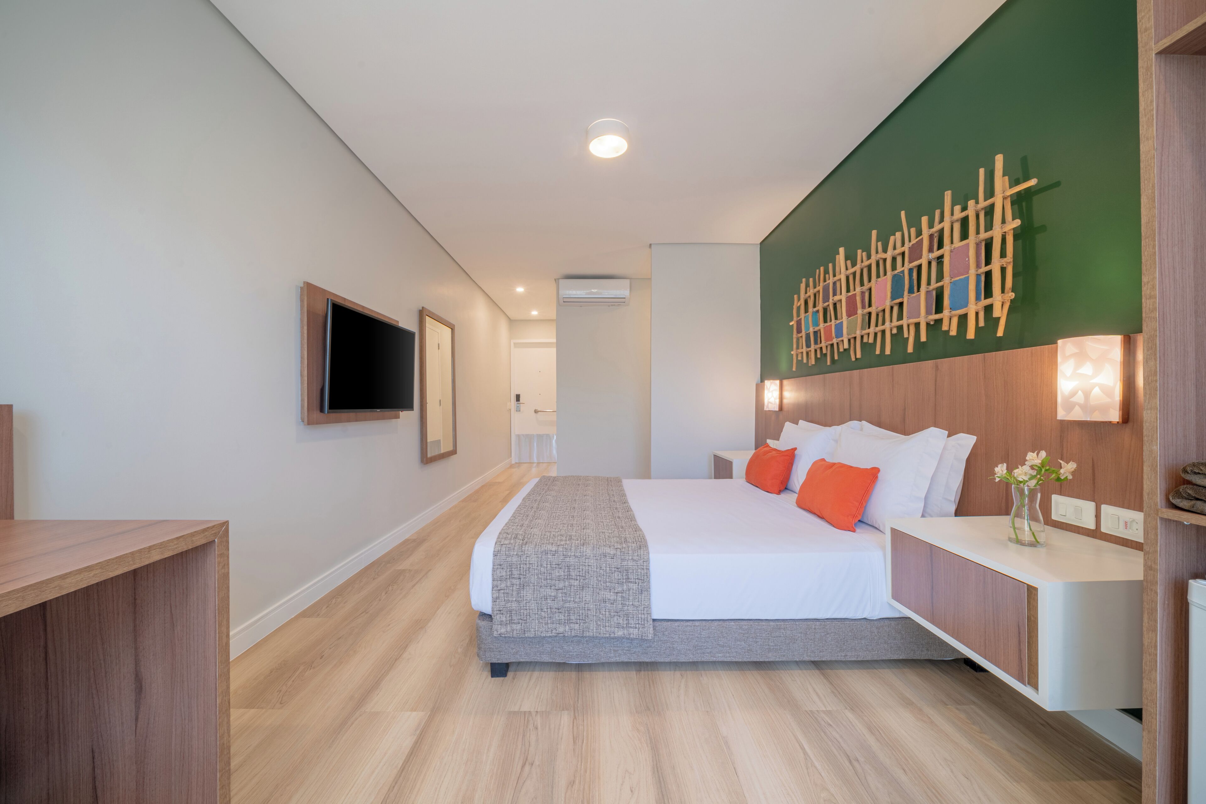 A modern hotel room with a large bed, a wooden desk, a flat-screen TV, and a green accent wall.