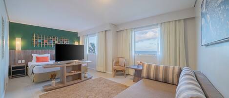 Una habitación de hotel moderna con cama, televisión, sofá, sillón y un ventanal con cortinas.
