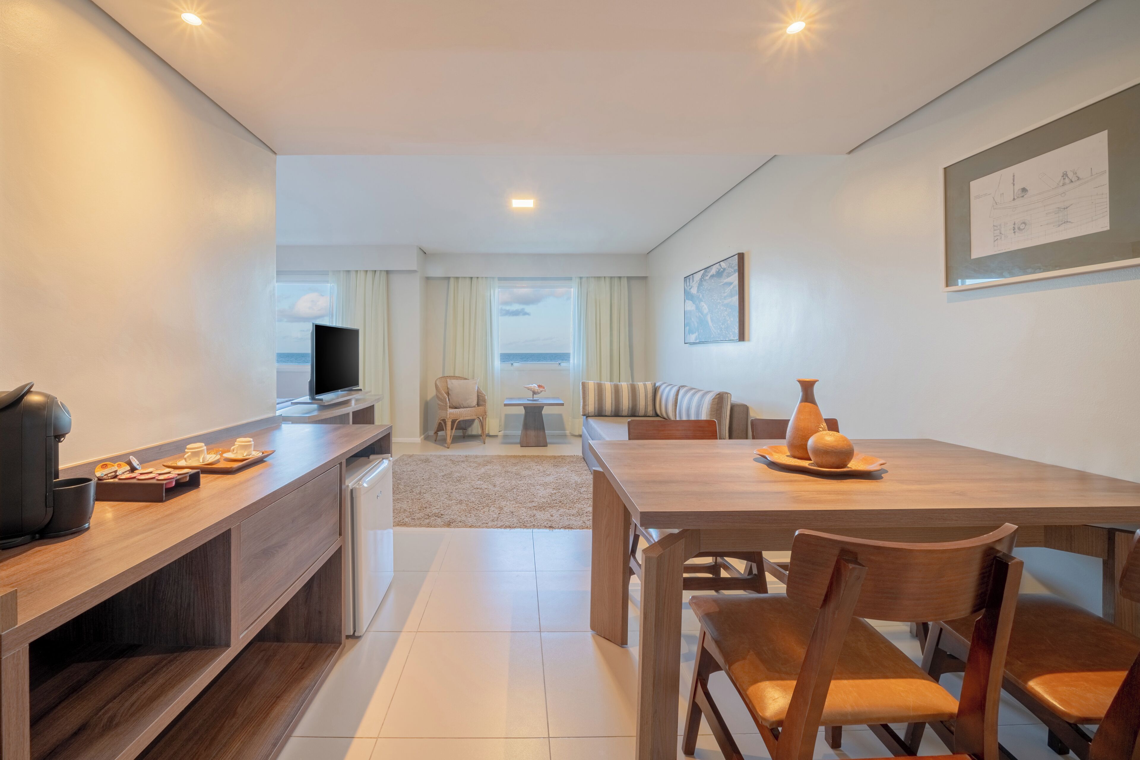 Una habitación de hotel moderna con una mesa de comedor de madera, un sofá, un televisor y vista al océano.