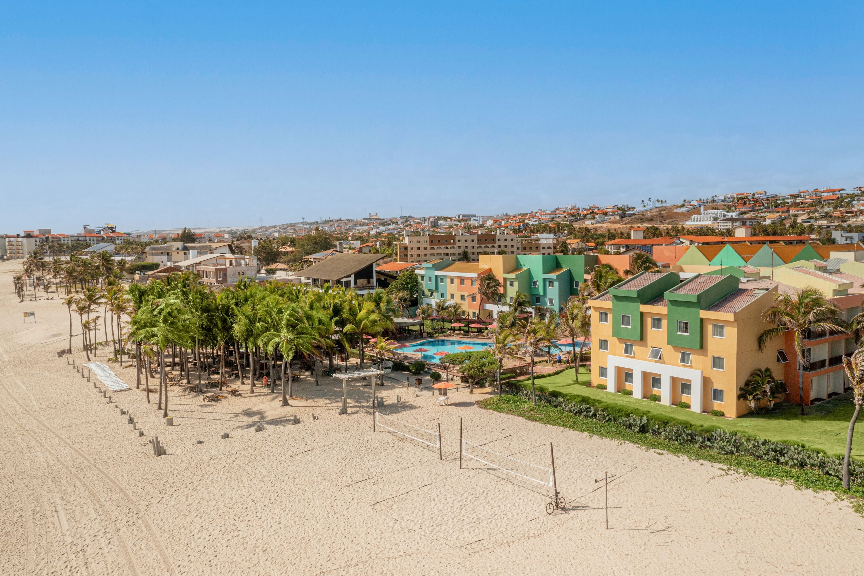 Ein Strandhotel mit Pool, Palmen und Sandstrand.