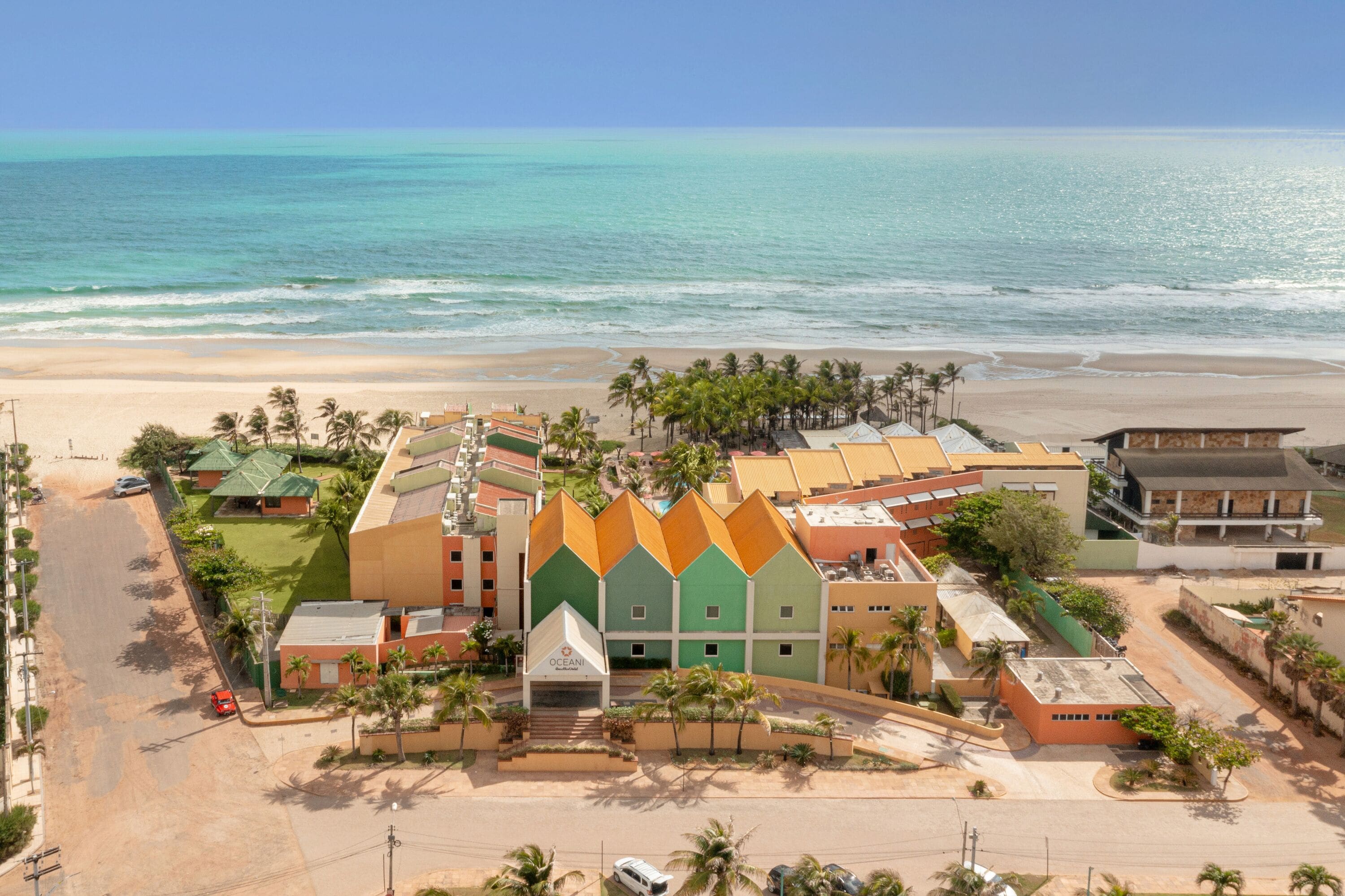 A beachfront hotel with a prominent green and orange building, a sandy beach, and a clear view of the ocean.