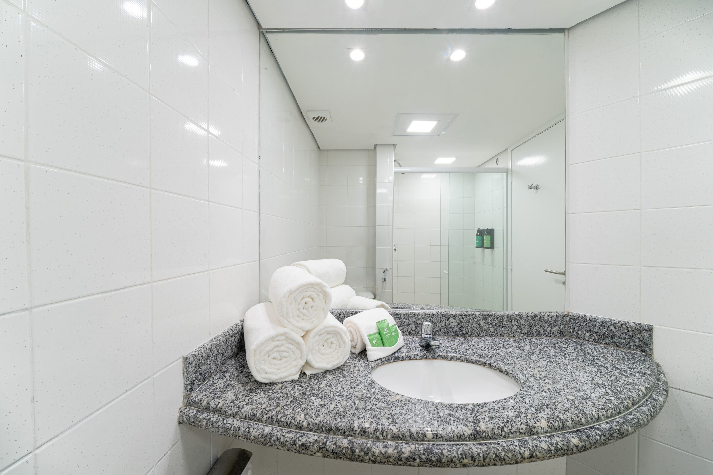 A modern bathroom with white tiled walls, a granite countertop, and a sink.