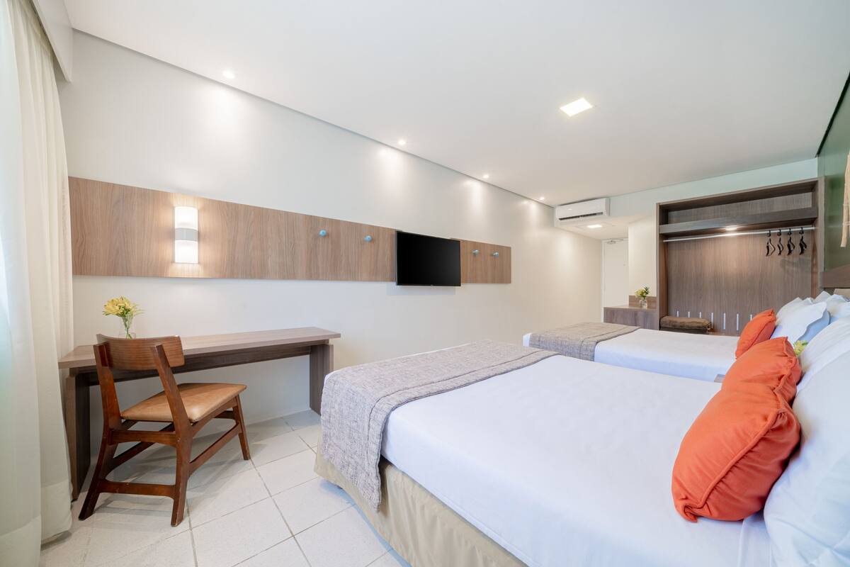 A modern hotel room with a desk, two beds, a TV, and a wardrobe.