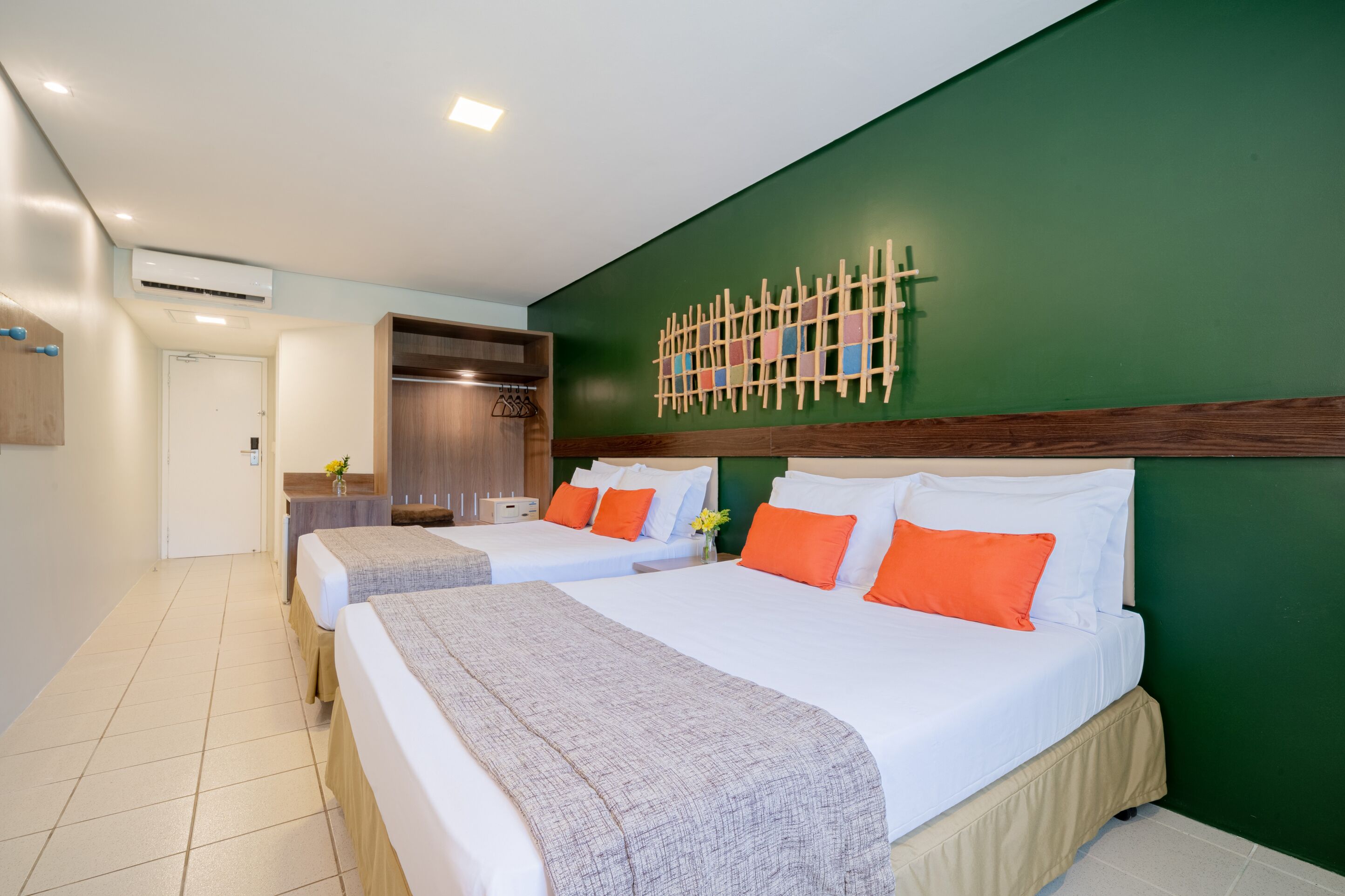 A hotel room with two beds, a green accent wall, and a wooden headboard.