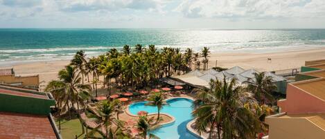 Resort com piscina, palmeiras e vista para a praia.