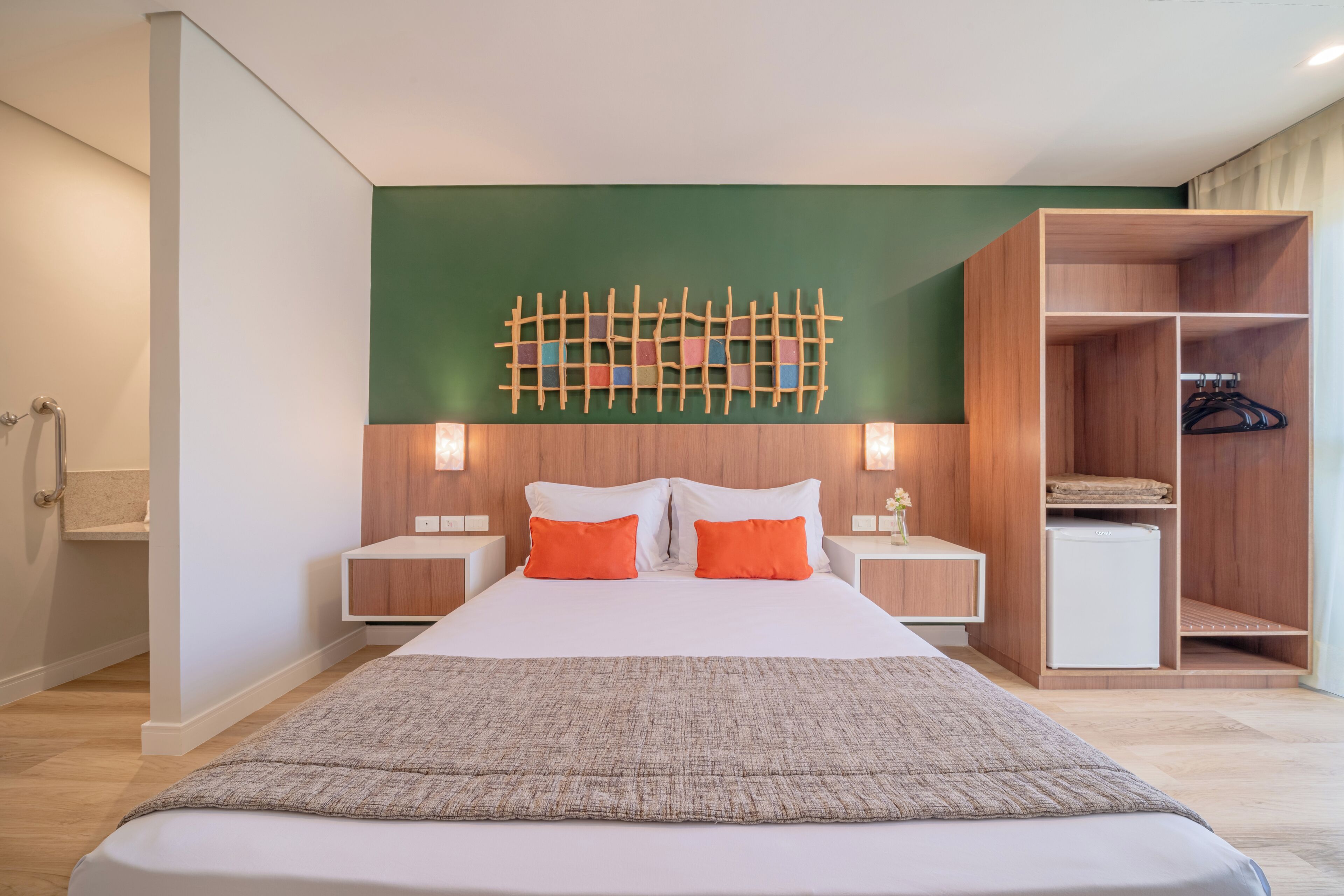 A modern hotel room with a large bed, wooden headboard, two nightstands, a wall-mounted artwork, and a built-in wardrobe.