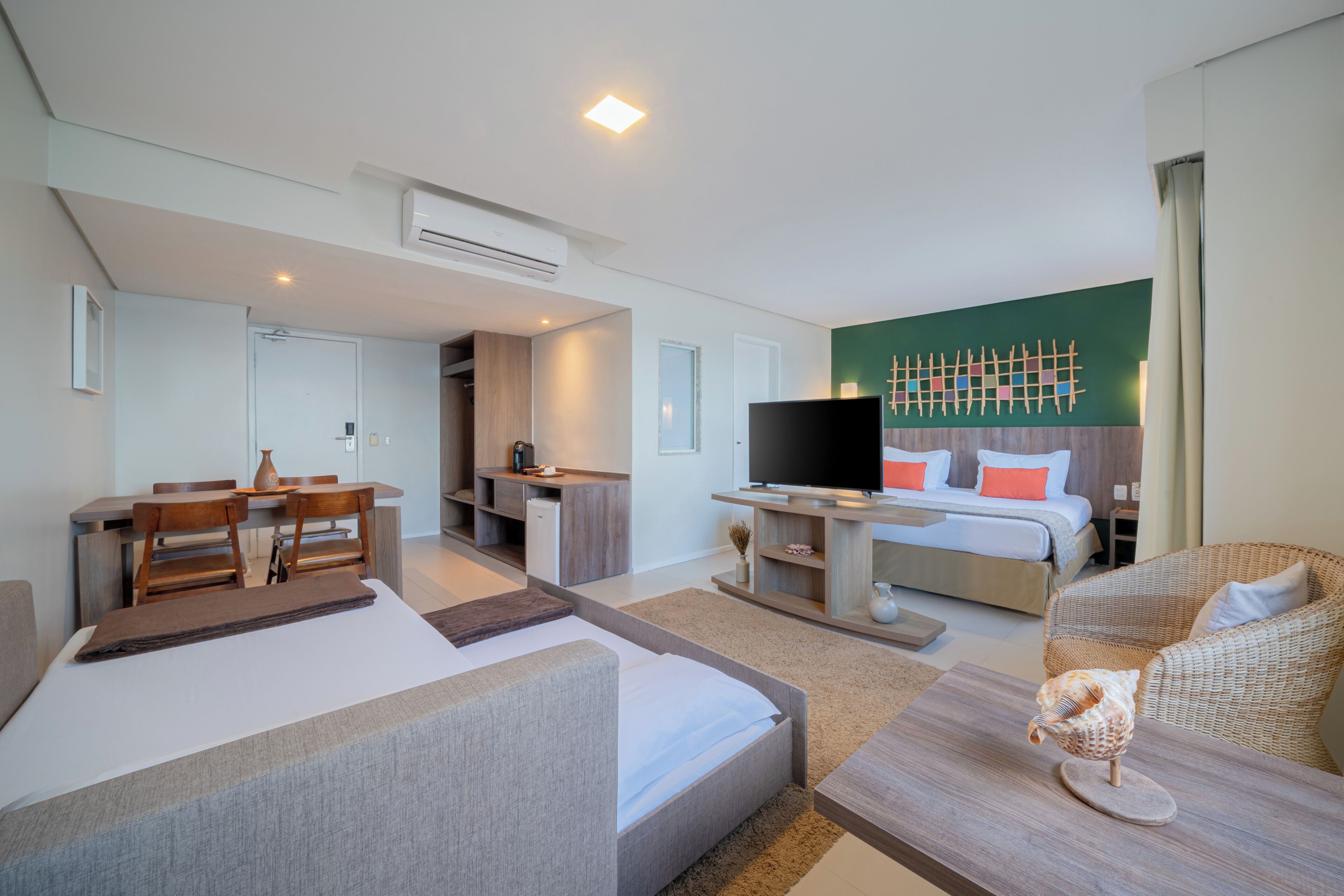 A modern hotel room with a bed, a desk, a television, and a dining area.