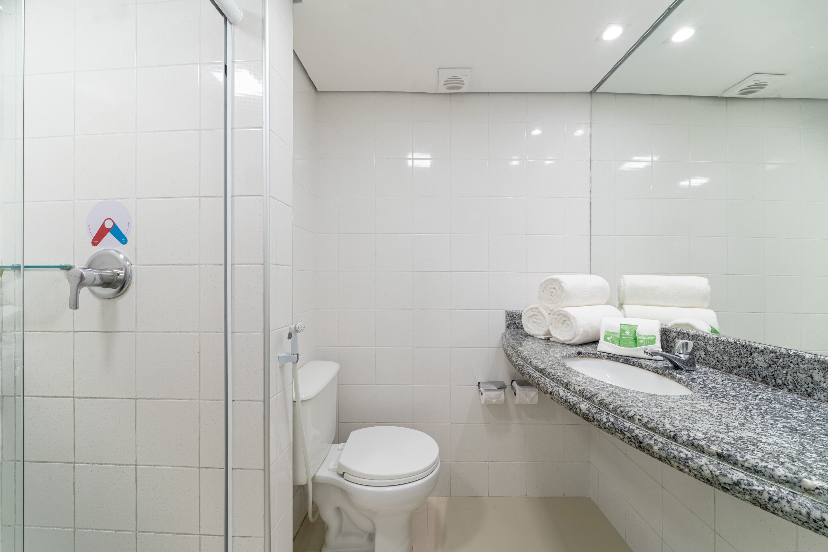 Ein modernes Badezimmer mit Duschabtrennung aus Glas, einer weißen Toilette und einer Waschtischplatte aus Granit mit Spüle und Ablage für Handtücher.