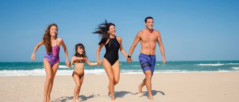 A family of four running on a sandy beach with the ocean in the background.