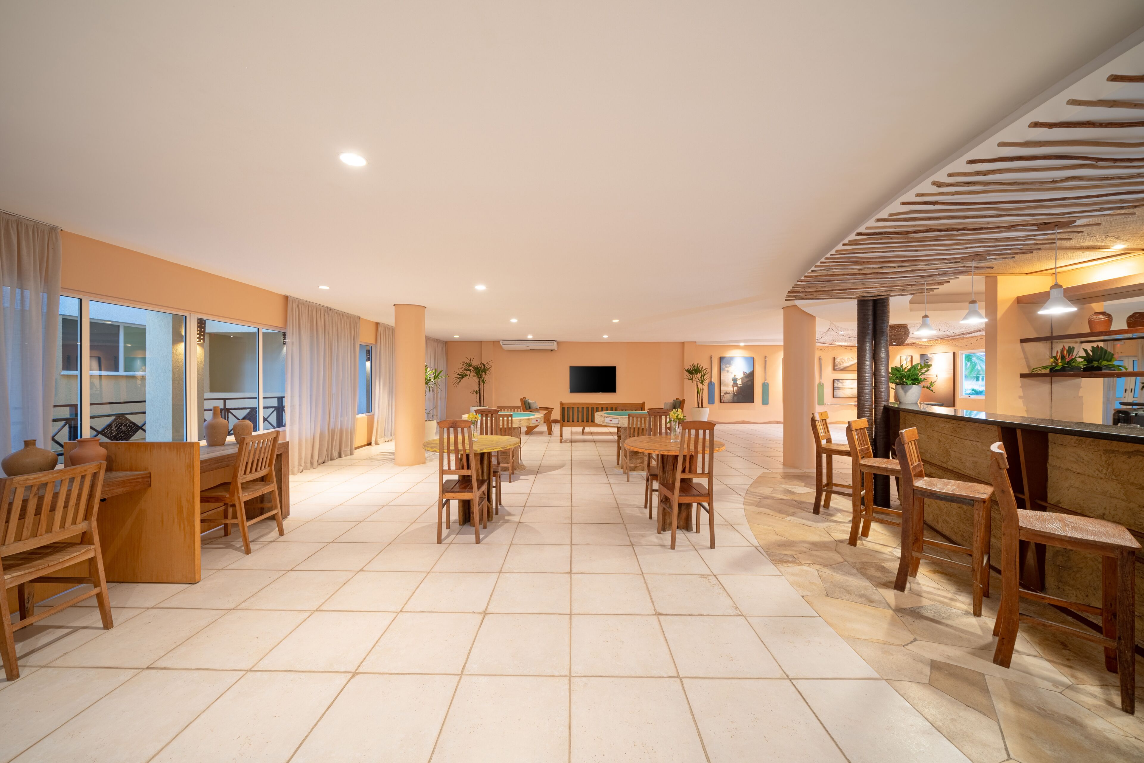 A spacious indoor area with multiple wooden tables and chairs, a flat-screen TV mounted on the wall, and a bar area with stools.