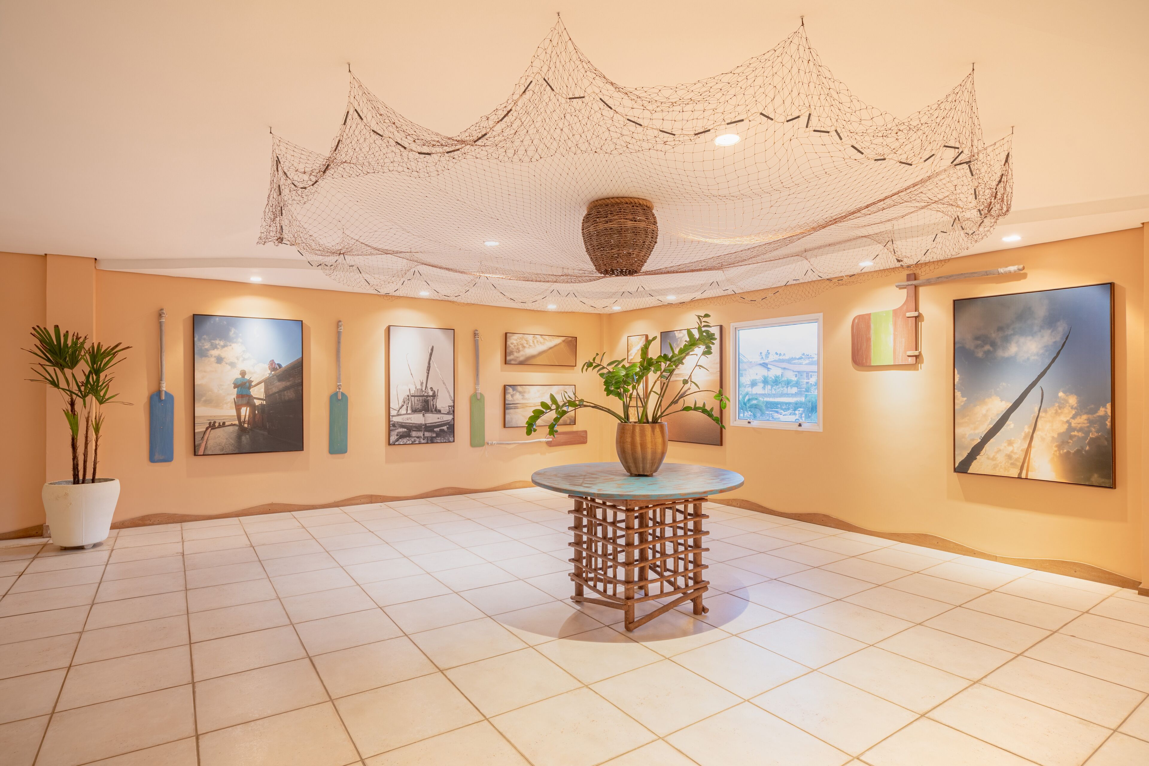 A spacious room with a tiled floor, a round wooden table with a vase, and multiple framed artworks on the walls.