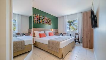 Habitación de hotel con dos camas, una pared de acento verde, un cabecero de madera, un televisor y vistas a palmeras.