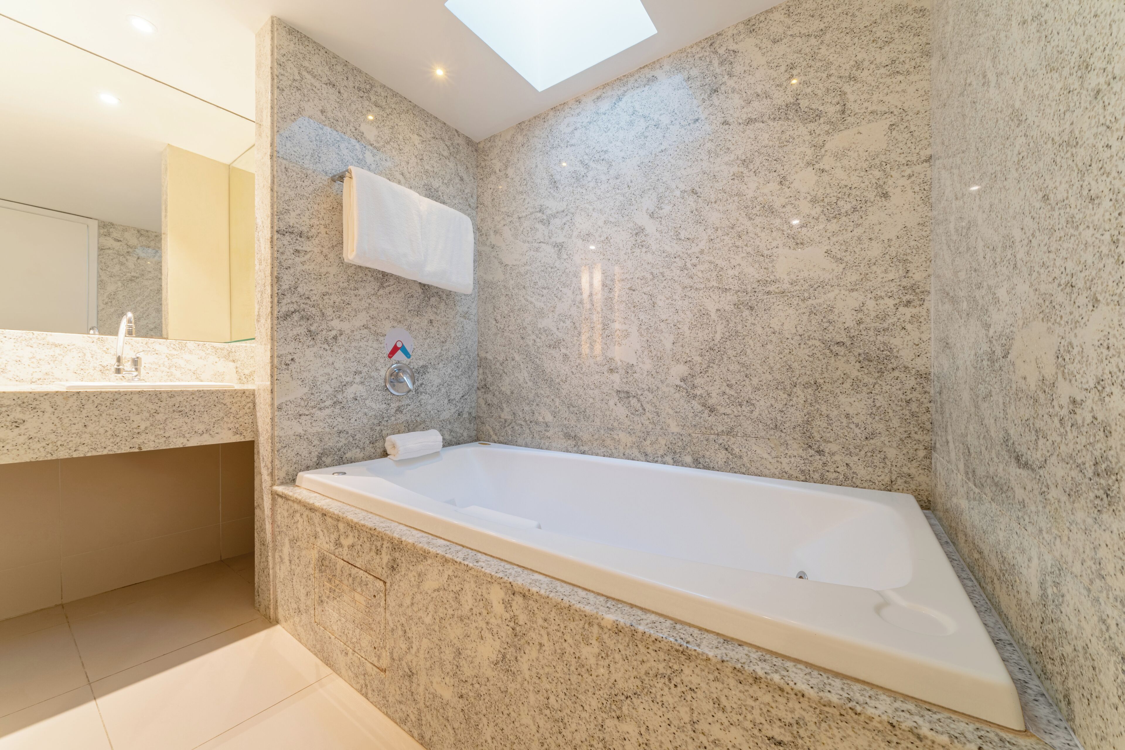Un baño moderno con una bañera grande, paredes de granito, un tragaluz y un espejo sobre el lavabo.