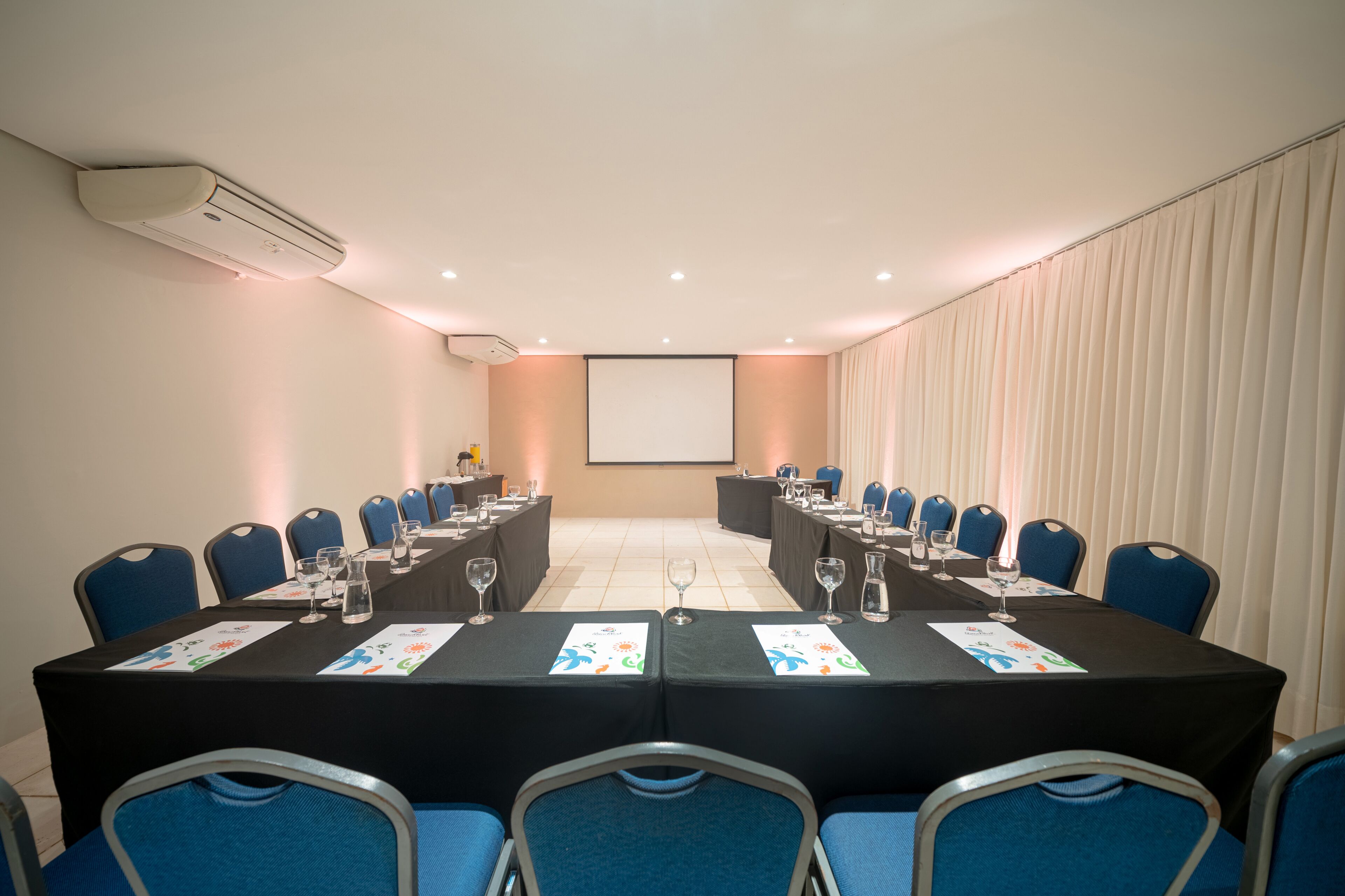 Un salón de conferencias con una larga mesa, sillas azules y una pantalla de proyector.