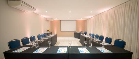 Un salón de conferencias con una larga mesa, sillas azules y una pantalla de proyector.