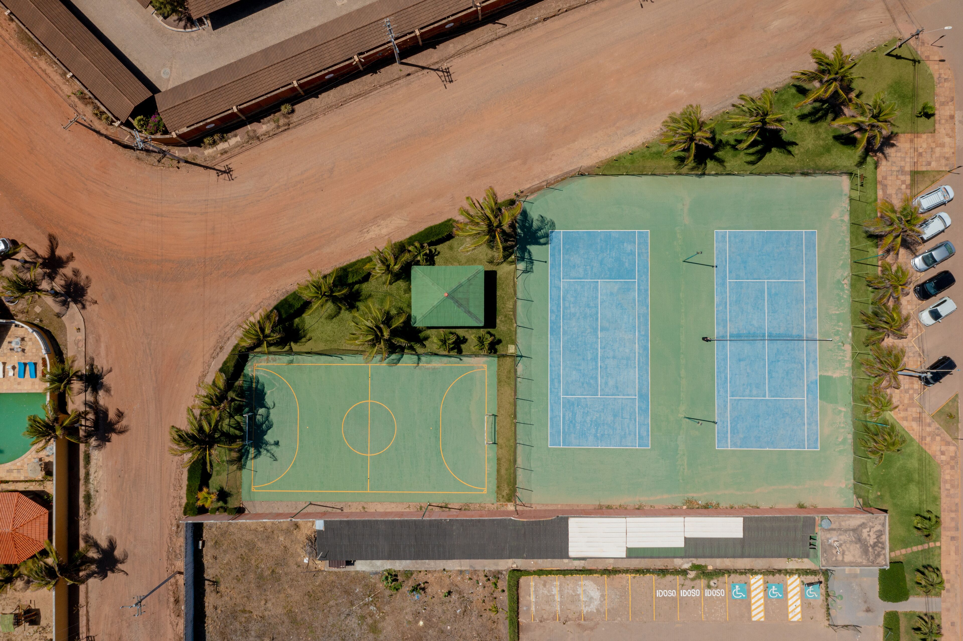 Vista aérea de un complejo deportivo con dos canchas de tenis, una cancha de baloncesto y un área de estacionamiento.