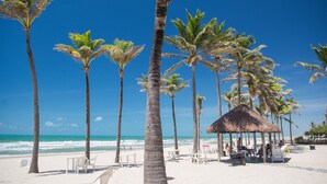 A beach with palm trees, a thatched-roof hut, and beach chairs. - Beach Park Oceani Resort (Aquiraz)