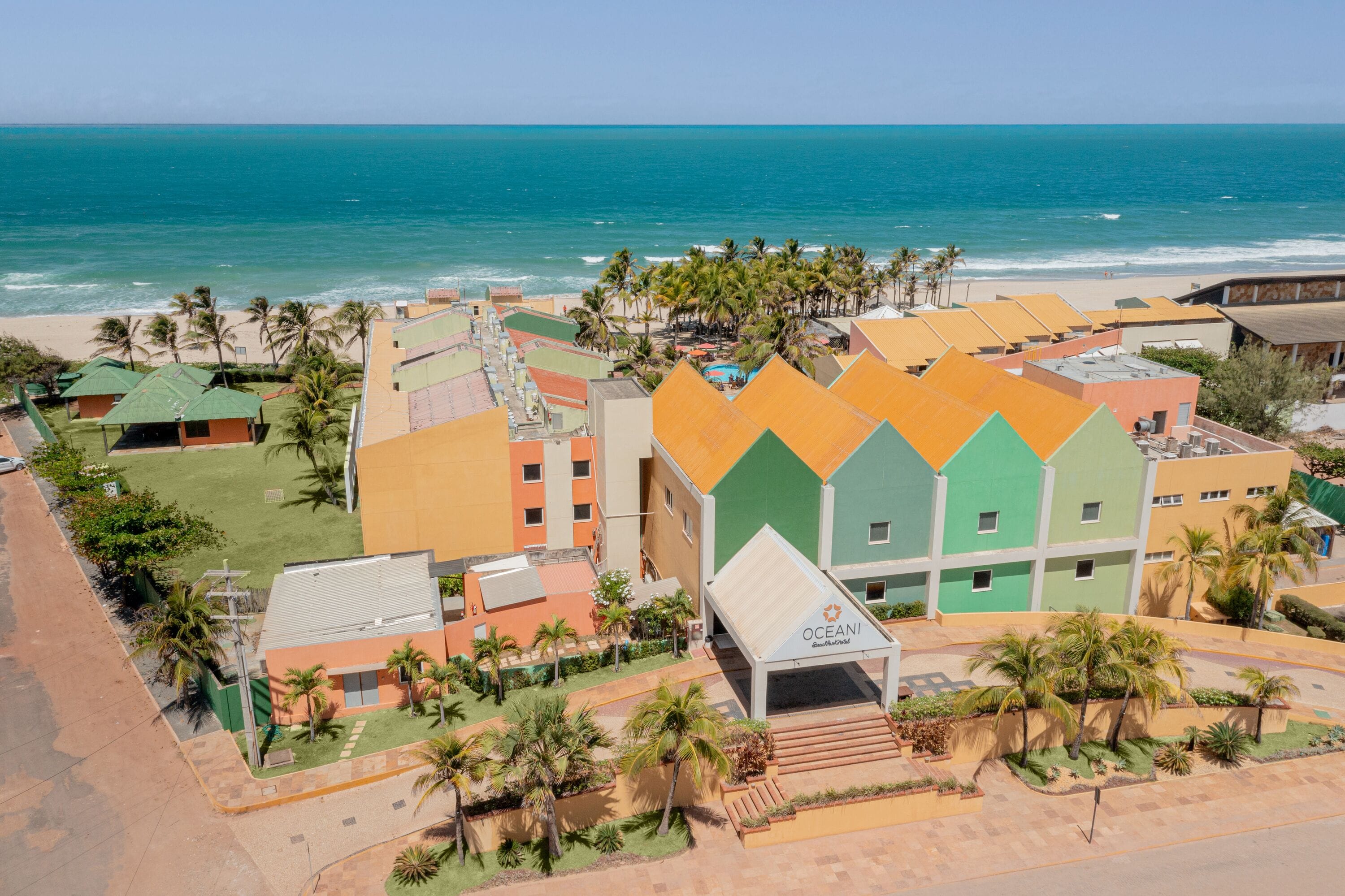 Un complexe hôtelier avec des bâtiments aux couleurs vives, un espace piscine et une vue sur la plage.