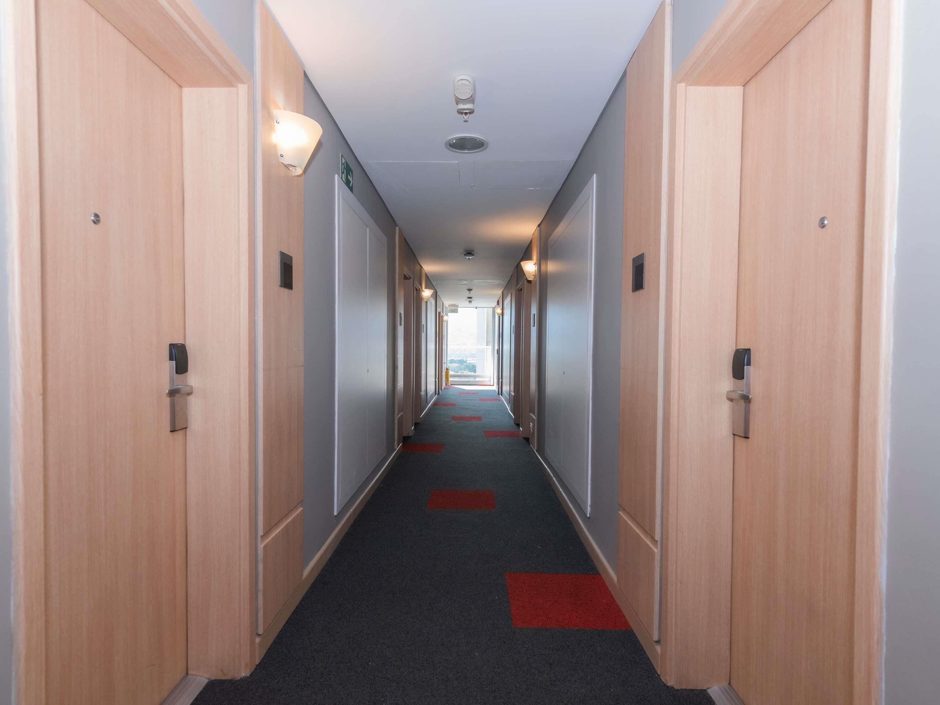Un pasillo de hotel con puertas de madera, suelo alfombrado y elegantes corredores rojos.